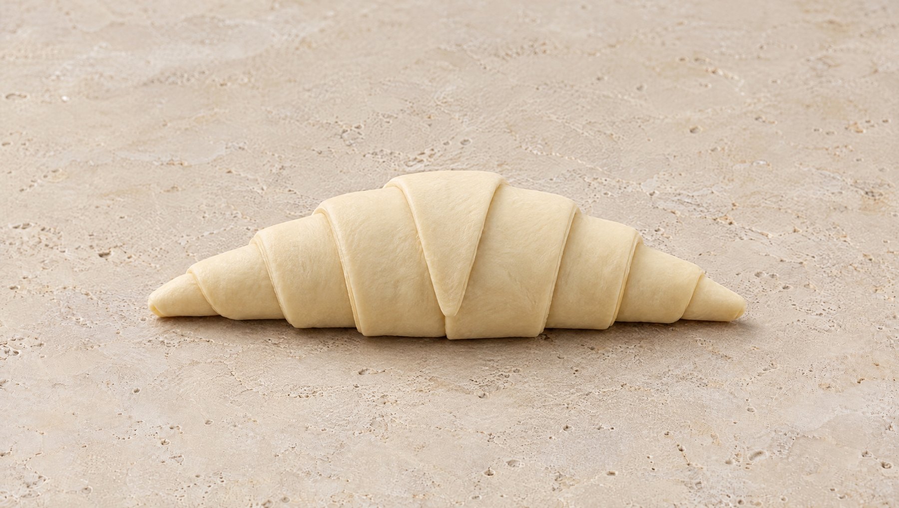 Croissant crudo ya enrollado, con la punta al frente